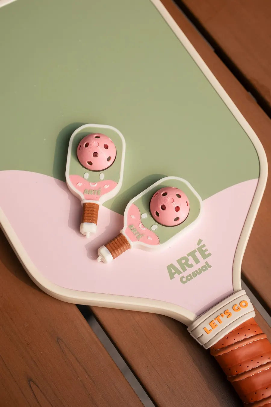 Two Bubbly Clicker charms resting on the face of an ARTÉ Casual paddle in matching green and pink