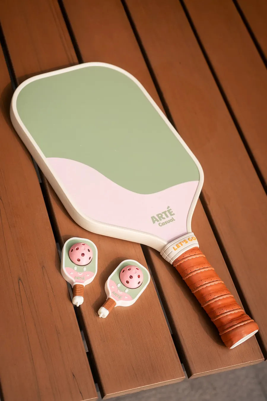 Two Bubbly Clicker charms on a wooden bench next to an ARTÉ Casual paddle with an orange grip